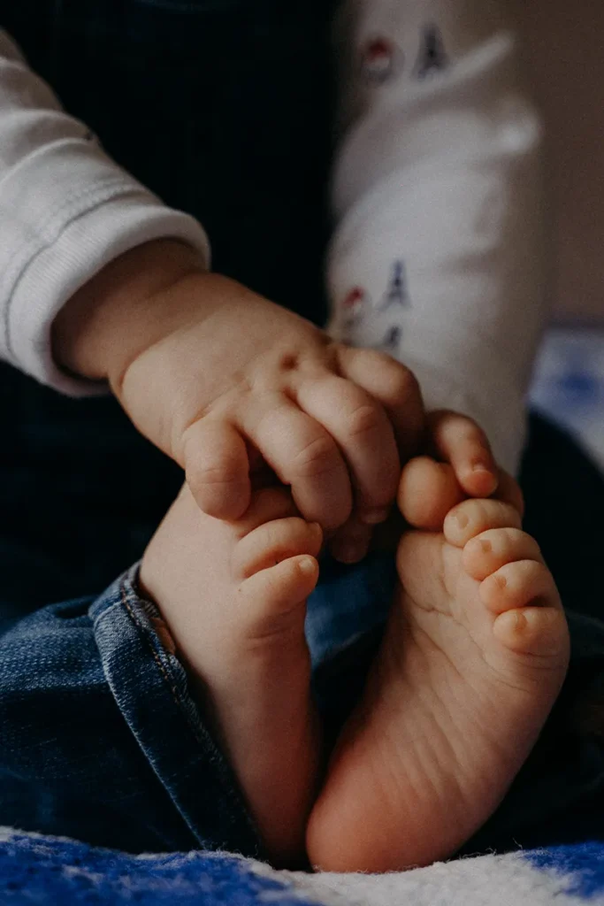 photographe bébé d'un détail d'une main de bébé tenant ses petits pieds