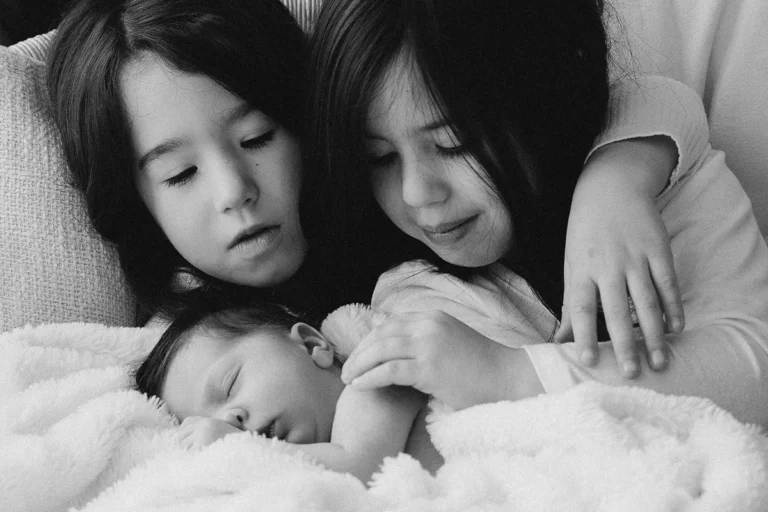 photographe bébé de deux soeurs câlinant leur petit frère tout bébé