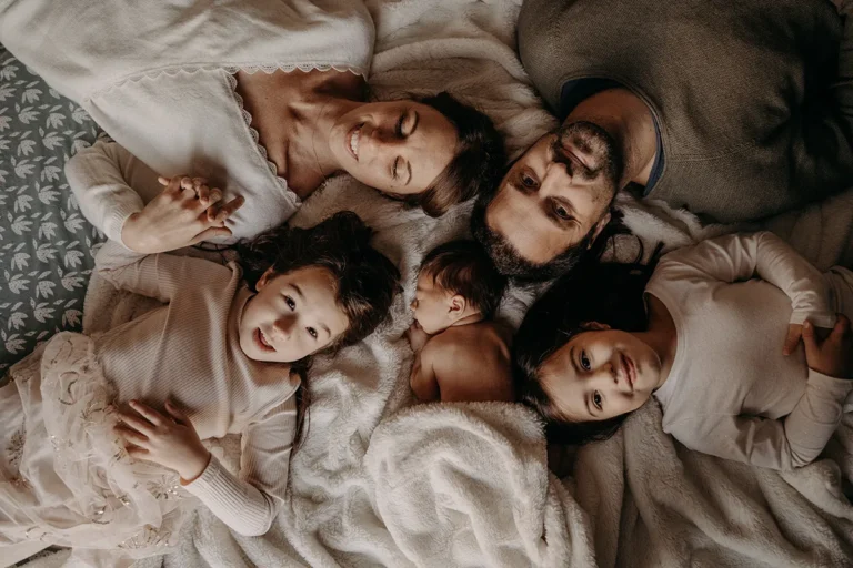 photographe bébé d'une famille allongée sur le lit entourant le nouveau né