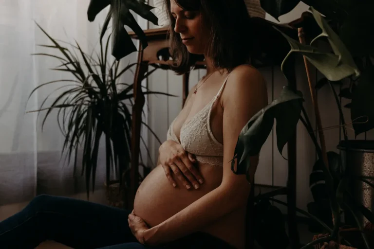 femme enceinte entourée de plantes photographiée en sous-vêtements assise dans son salon par une photographe grossesse