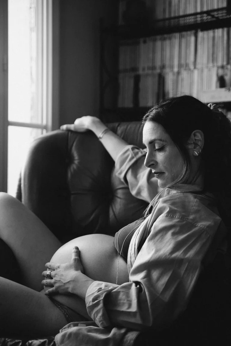 photographe grossesse d'une femme enceinte sur son fauteuil dans son salon le ventre nu