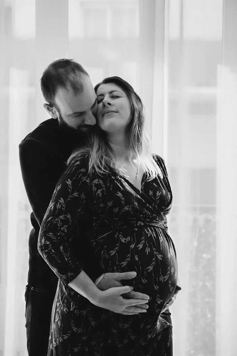 une femme enceinte enlacée par son chéri, ils sont photographié dans leur salon par une photographe grossesse