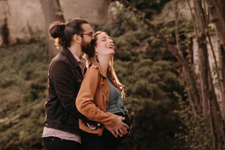 photographe grossesse de futurs parents qui rient pendant leur séance grossesse dans la nature