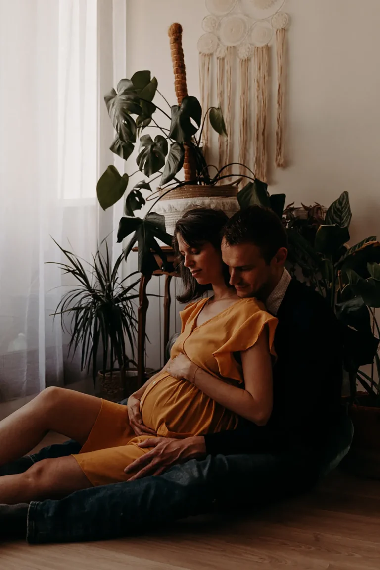 photographe grossesse de futurs parents assis enlacés dans leur salon