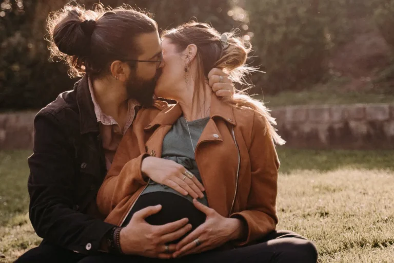 photographe grossesse de futurs parents qui s'embrassent en tenant le ventre de la femme enceinte assis dans un parc