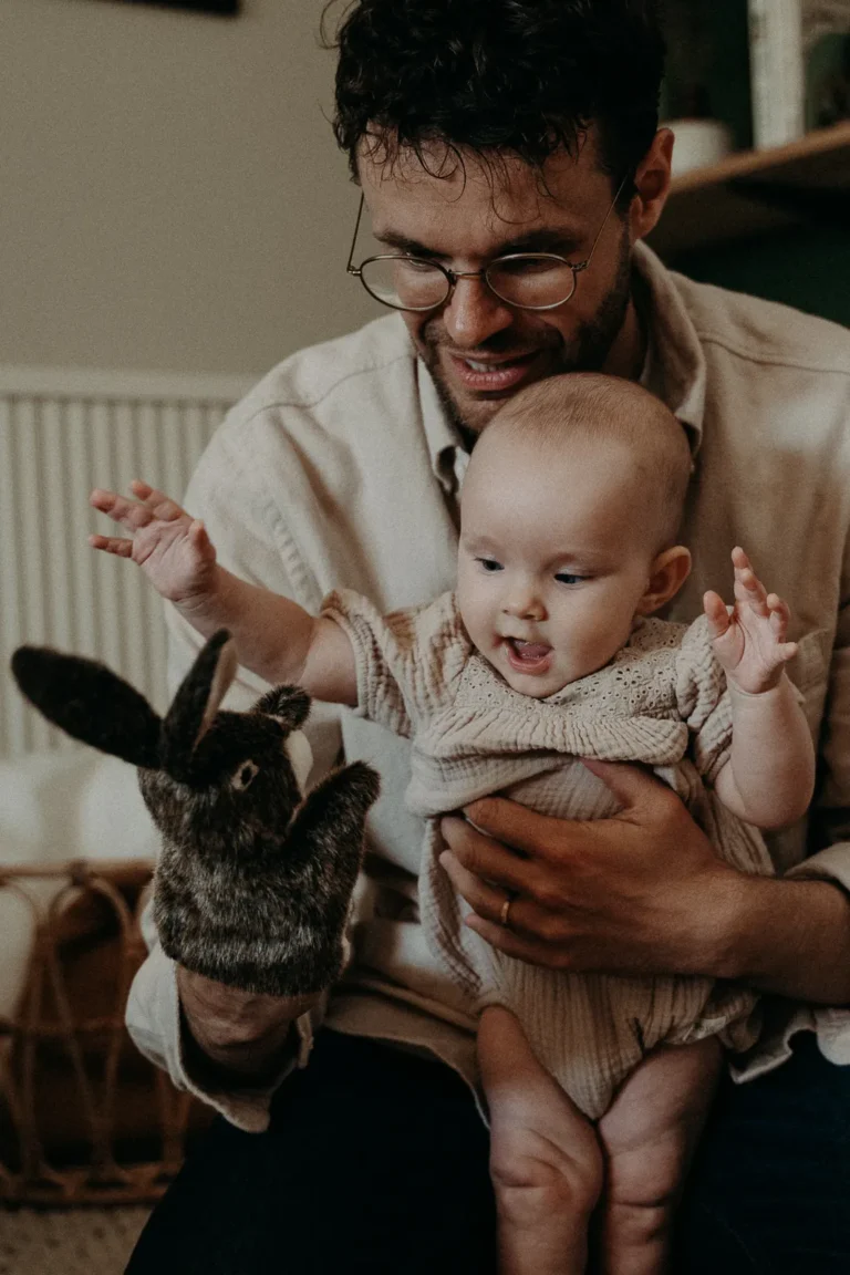 bébé dans les bras de son père jouant avec une peluche photographiés par une photographe bébé