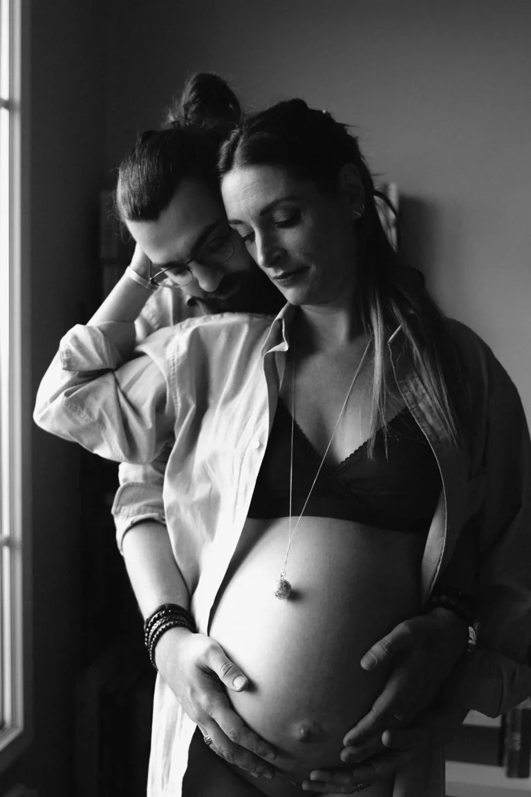 femme enceinte enlacée par son amoureux qui caresse son ventre nu photographiés par une photographe grossesse à paris