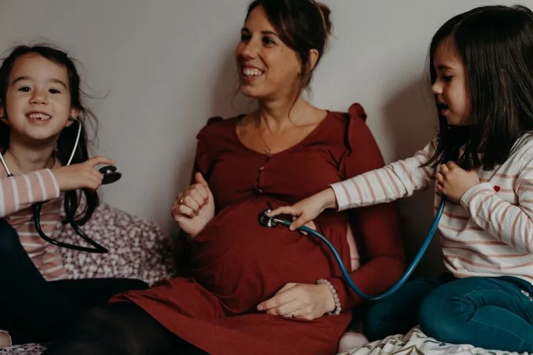 maman enceinte avec ses deux petites filles qui écoutent le bébé dans son ventre photographié par une photographe grossesse à Paris