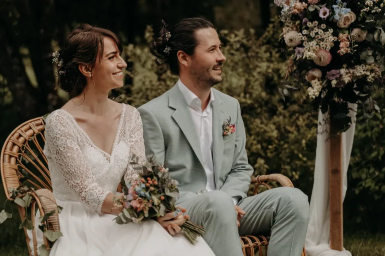 mariés souriant sur un banc en osier lors de leur cérémonie laïque photographiés par une photographe de mariage