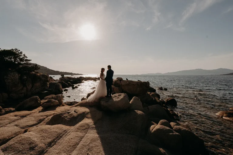 mariés se tenant la main face à face sur des rochers devant la mer photographiés par une photographe de mariage