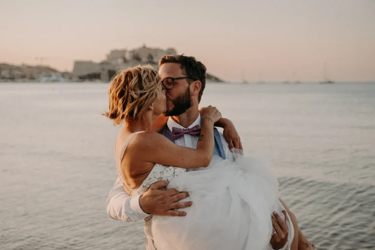 marié porte sa femme et l'embrasse devant la mer photographiés par une photographe de mariage